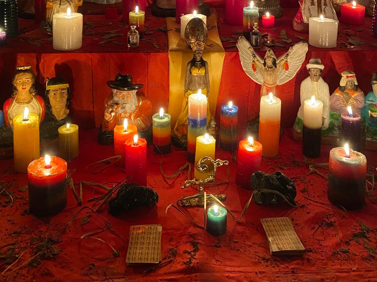 Mi altar: veladoras encendidas, figuras y dos barajas sobre un mantel rojo.
