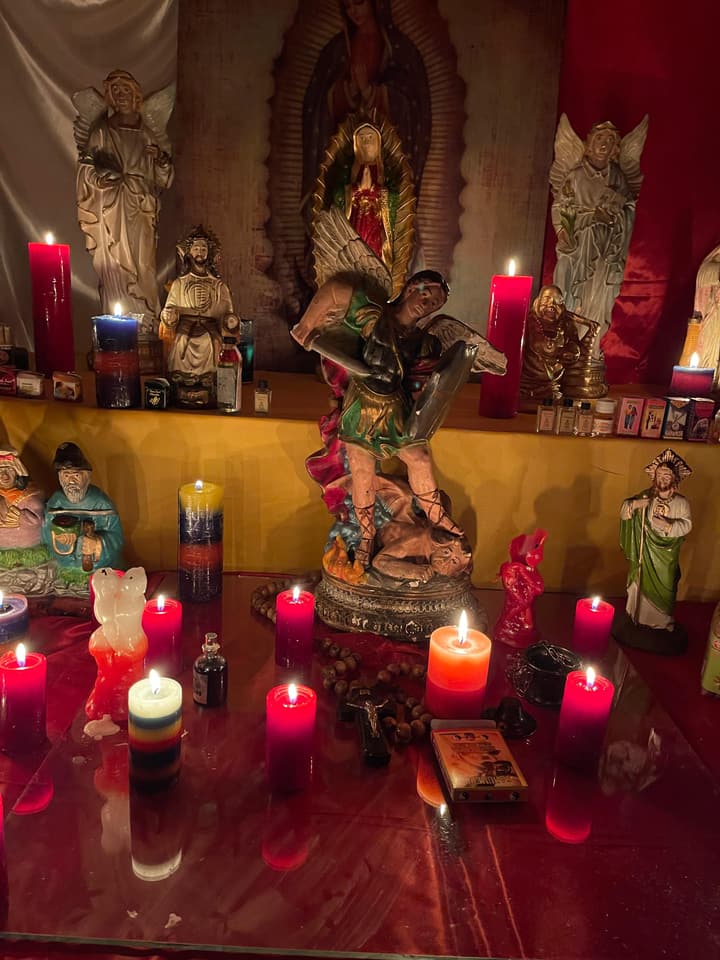 San Miguel Arcángel en mi altar, rodeado de veladoras rojas y de colores.
