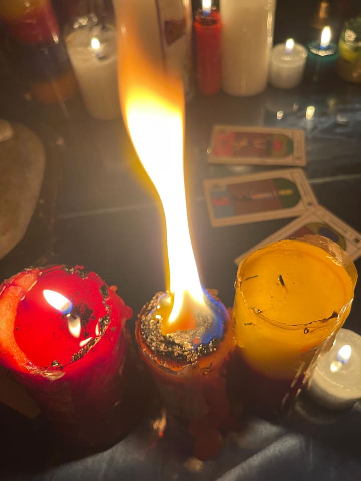Una veladora encendida con la llama alta en mi altar, junto a otras velas y cartas de tarot.